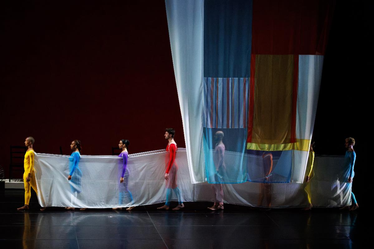 A group of people in leotards holding a white sheet

Description automatically generated